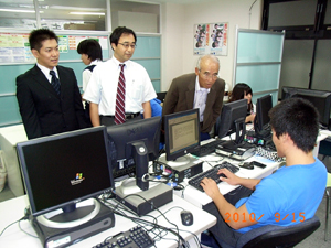 写真：PCを使う生徒に話を聞く住信AMの佐藤調査役と日野理事長
